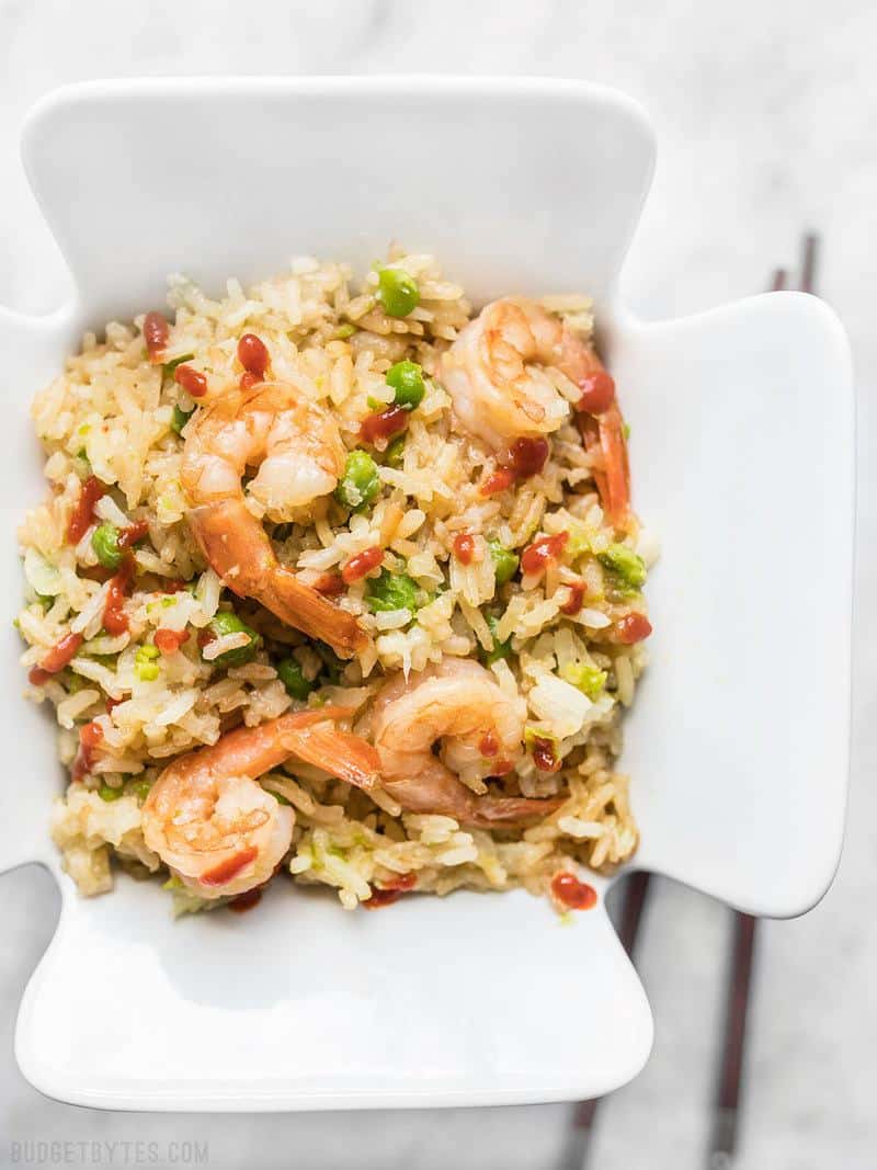 Close up of Teriyaki Shrimp and Rice in a ceramic takeout container, topped with sriracha