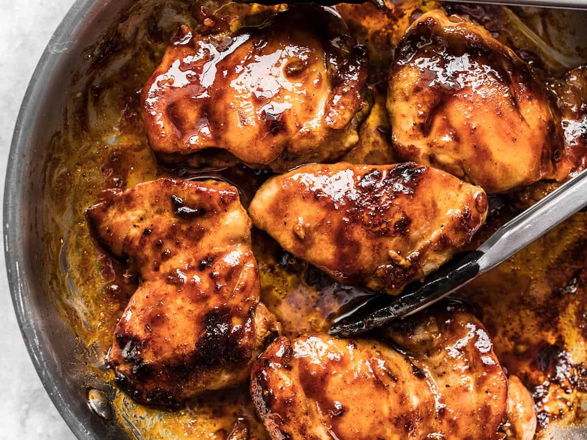 close up of glazed chicken in a skillet with tongs