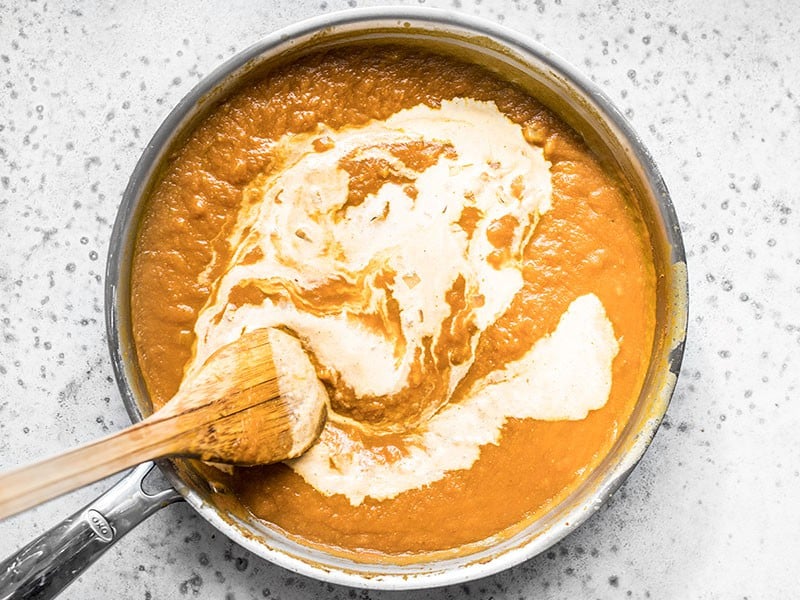 Heavy Cream being stirred into the Simmered Sauce with a wooden spoon