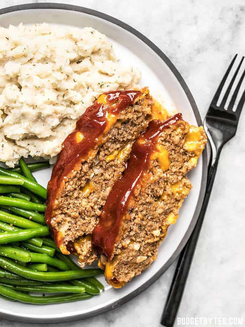 Two Slices of Cheddar Cheeseburger Meatloaf with mashed potatoes and green beans.