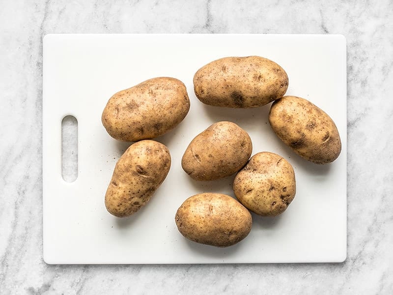 Seven Russet Potatoes on a white cutting board