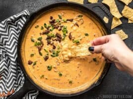 A chip being dipped into a skillet full of Spicy Chorizo Cheese Dip