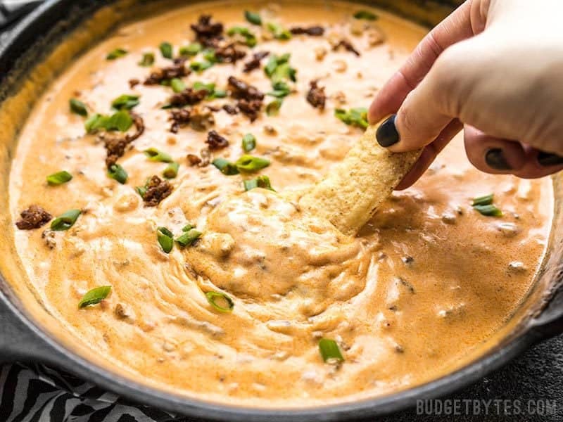 Close up of a chip being dipped into Spicy Chorizo Cheese Dip