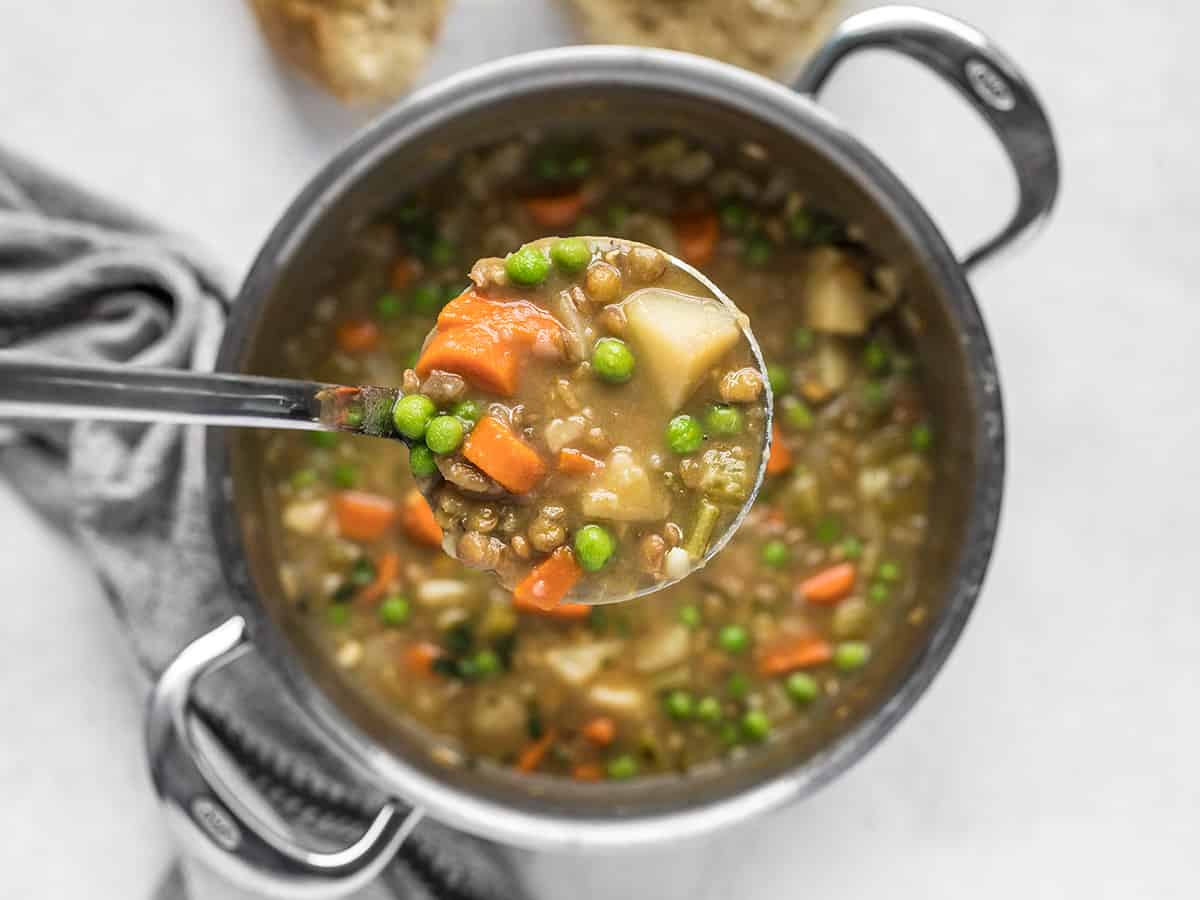 A ladle full of lentil stew held above the pot.