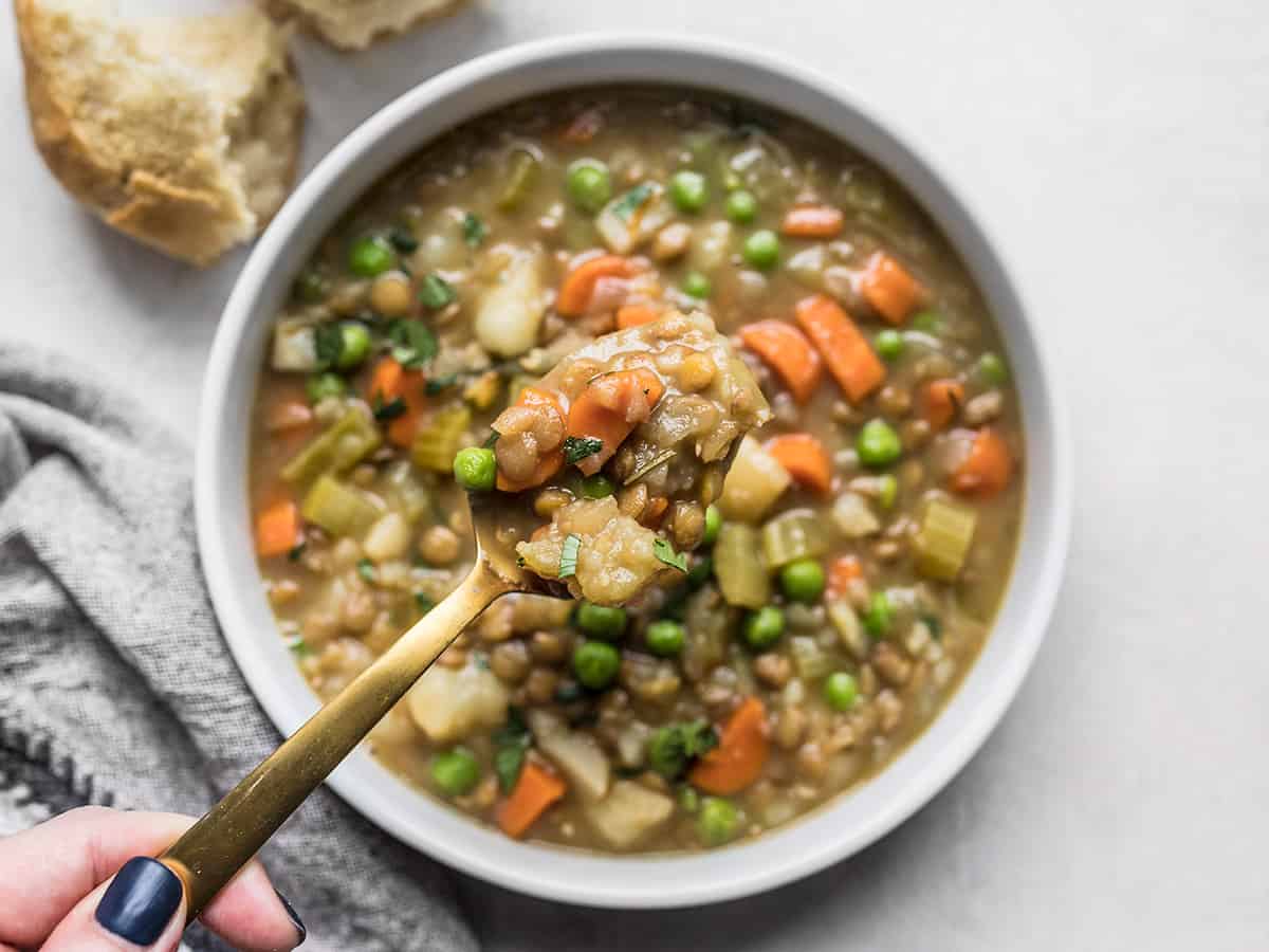 A hand lifting a spoonful of lentil stew out of the bowl. 