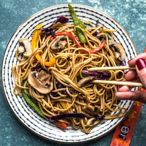 Lo Mein on a plate with someone digging in with chopsticks.