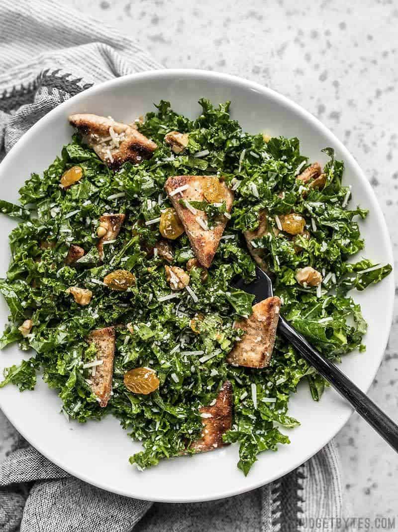 A big bowl full of Kale Salad with Toasted Pita, Parmesan, Walnuts, and Golden Raisins.