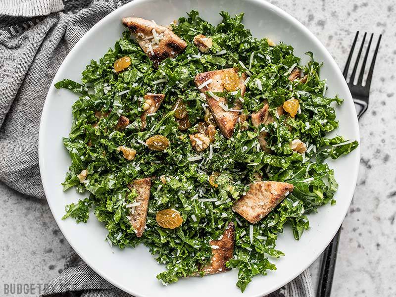 A plate full of Kale Salad with Toasted Pita, Parmesan, Walnuts, and Golden Raisins