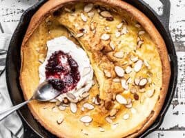 Close up of jam being spread on ricotta inside a baked Almond Dutch Baby