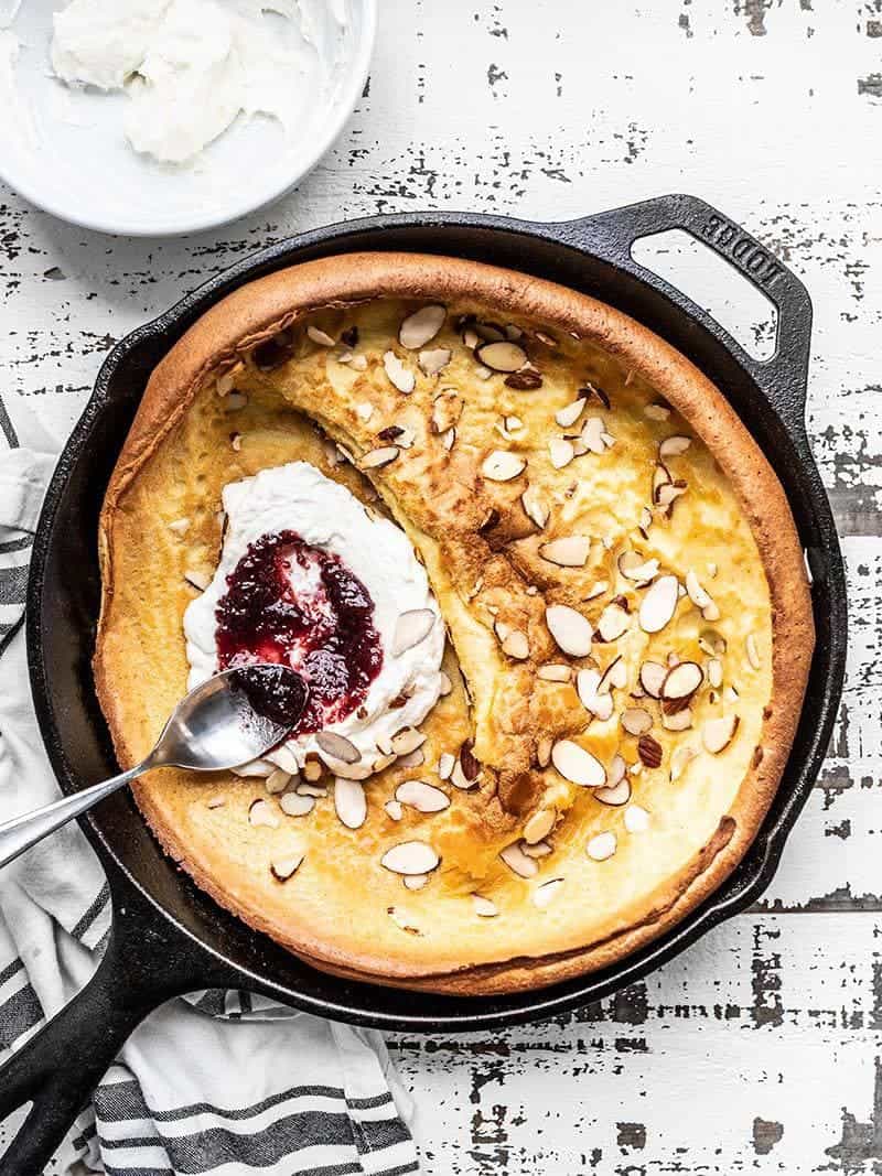 An Almond Dutch Baby with Ricotta and Jam in a cast iron skillet ready to slice and serve.