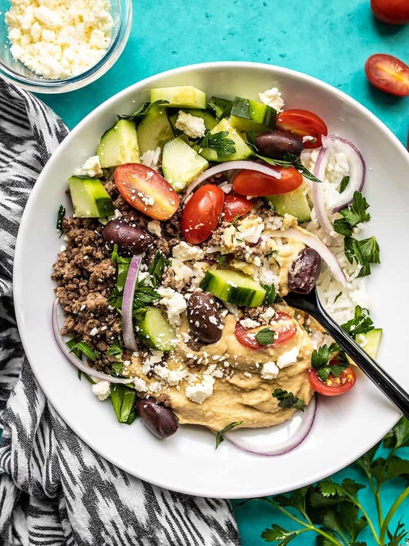 A Mediterranean Hummus Bowl about to be eaten with extra feta and tomatoes on the side.