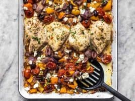 Sheet Pan Greek Chicken and Vegetables being scooped off the sheet pan with a spatula.