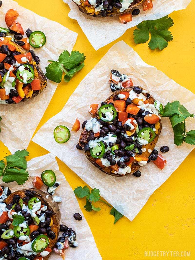 Loaded Sweet Potatoes with Lime Crema on parchment paper with a yellow background