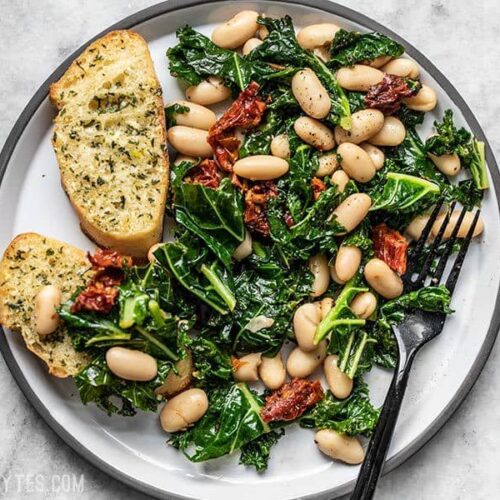 A plate full of Sun Dried Tomato, Kale, and White Bean Skillet with garlic bread