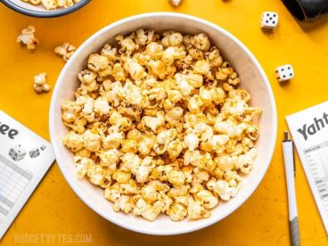 A big white bowl of Sriracha Nooch Popcorn next to dice and other game pieces