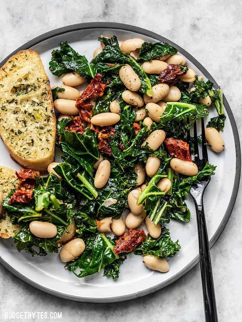 Close up of a plate full of Sun Dried Tomato, Kale, and white Bean Skillet with Garlic Bread