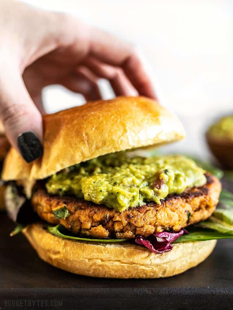 A Cajun Salmon Burger with guacamole being topped with the top half of a bun