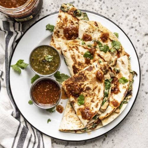 A plate of Creamy Chicken and Spinach Quesadillas with two dishes of salsa and a cilantro garnish