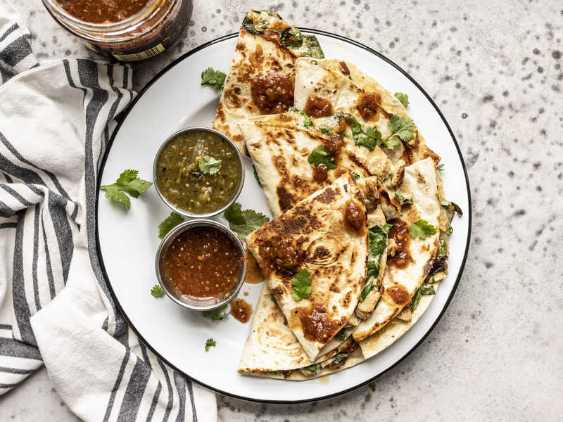 A plate of Creamy Chicken and Spinach Quesadillas with two dishes of salsa and a cilantro garnish