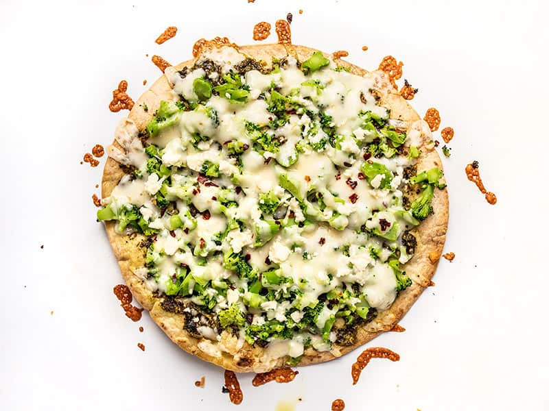 Baked Broccoli Pesto Pizza on the baking sheet with browned cheese around the edges.