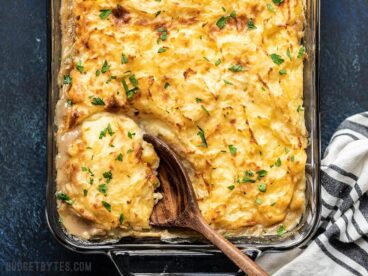 Overhead view of a wooden spoon scooping out a portion of Cheesy Cottage Pie from the casserole dish