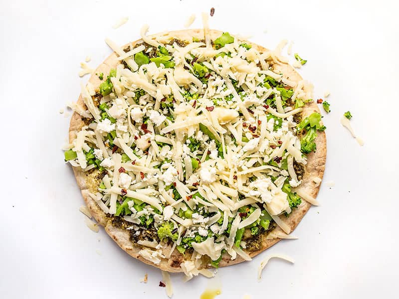 Fully topped broccoli pesto pizza ready to go back into the oven