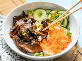 Front view of chopsticks picking up a slice of mushroom out of a Gochujang Mushroom Bowl.