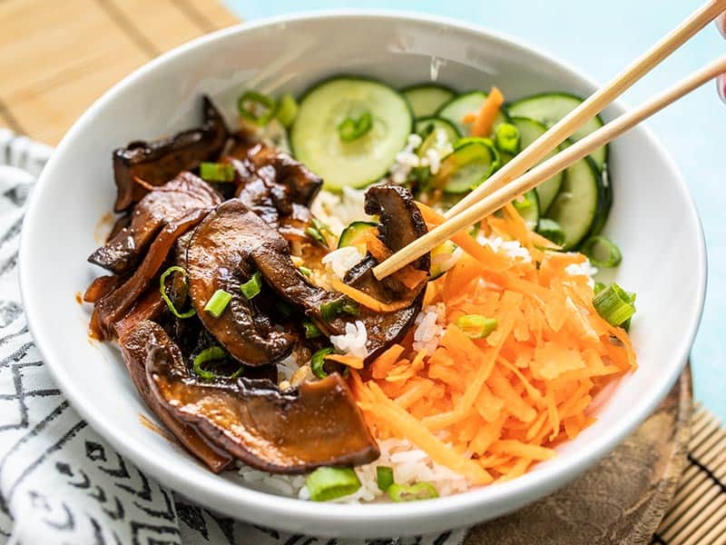 Front view of chopsticks picking up a slice of mushroom out of a Gochujang Mushroom Bowl.