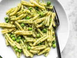 Parsley Pesto Pasta with Peas in a white bowl with a black fork in the side.