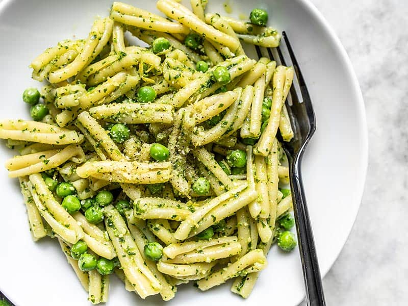 Parsley Pesto Pasta with Peas in a white bowl with a black fork in the side.