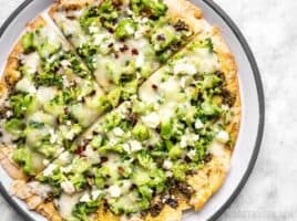 Close up of a Quick Fix Broccoli Pesto Pizza on a plate with crushed red pepper sprinkled on top.