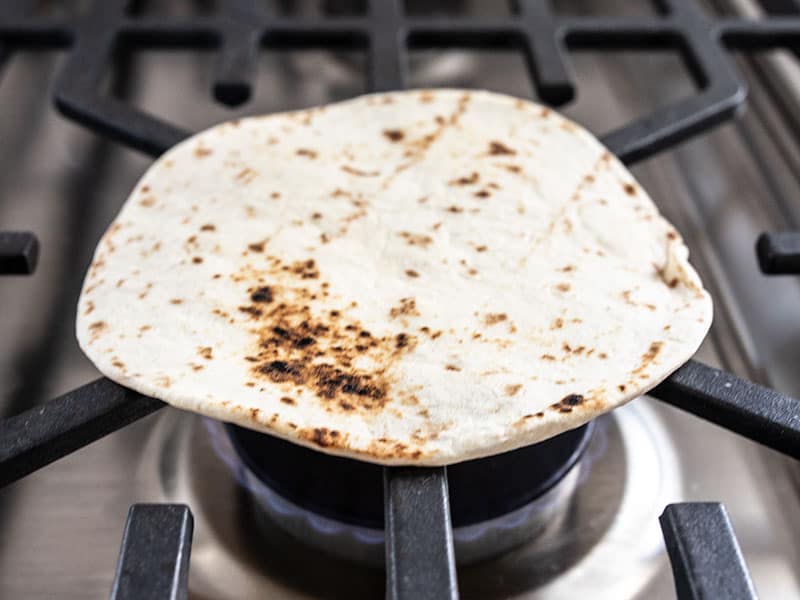 A flour tortilla being toasted over an open gas flame