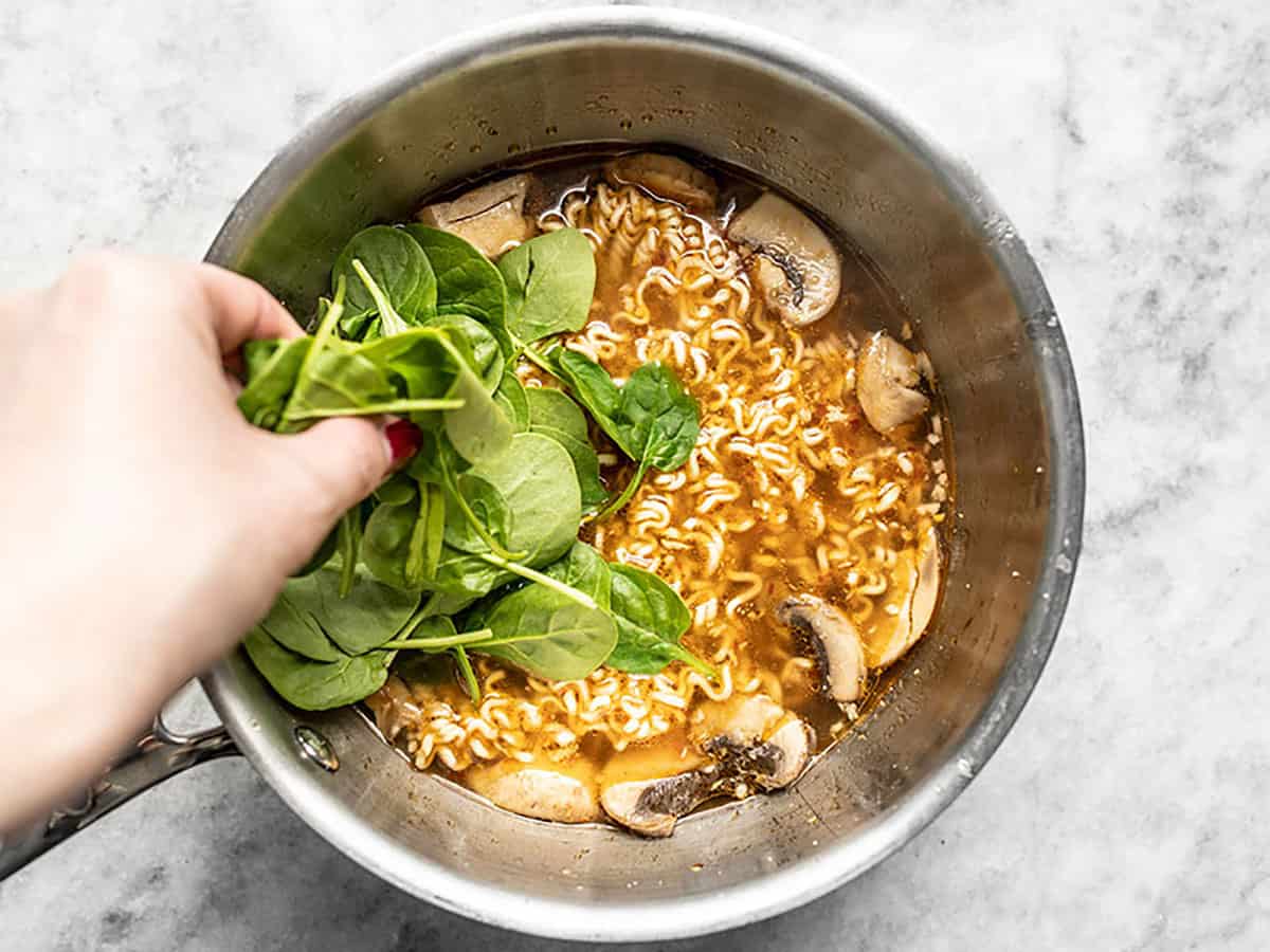 Fresh spinach being added to a pot of instant ramen. 