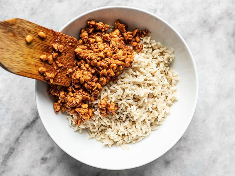 Tempeh being scooped onto a bowl of rice