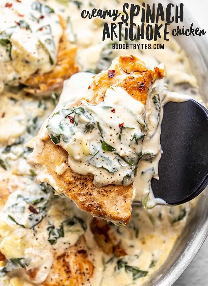 A spatula lifting one piece of Creamy Spinach Artichoke Chicken out of the skillet.