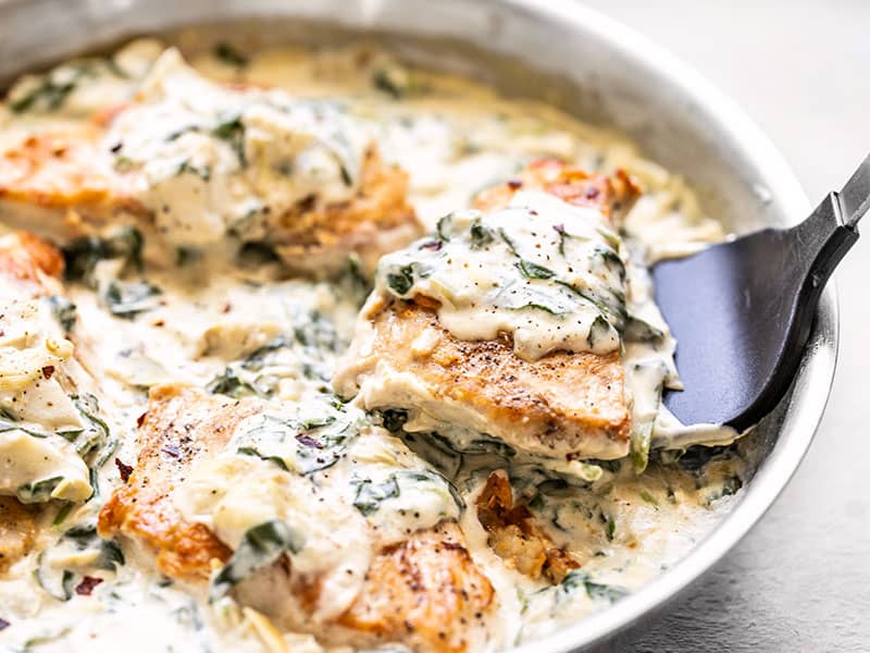 A piece of Creamy Spinach Artichoke Chicken being lifted out of the skillet with a spatula, side view