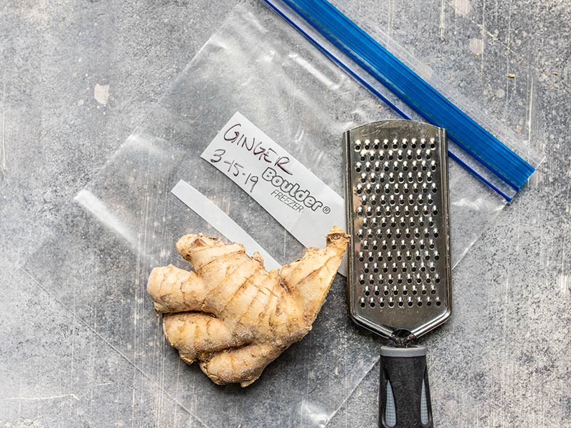 Fresh ginger root next to a cheese grater, laying on a freezer bag.