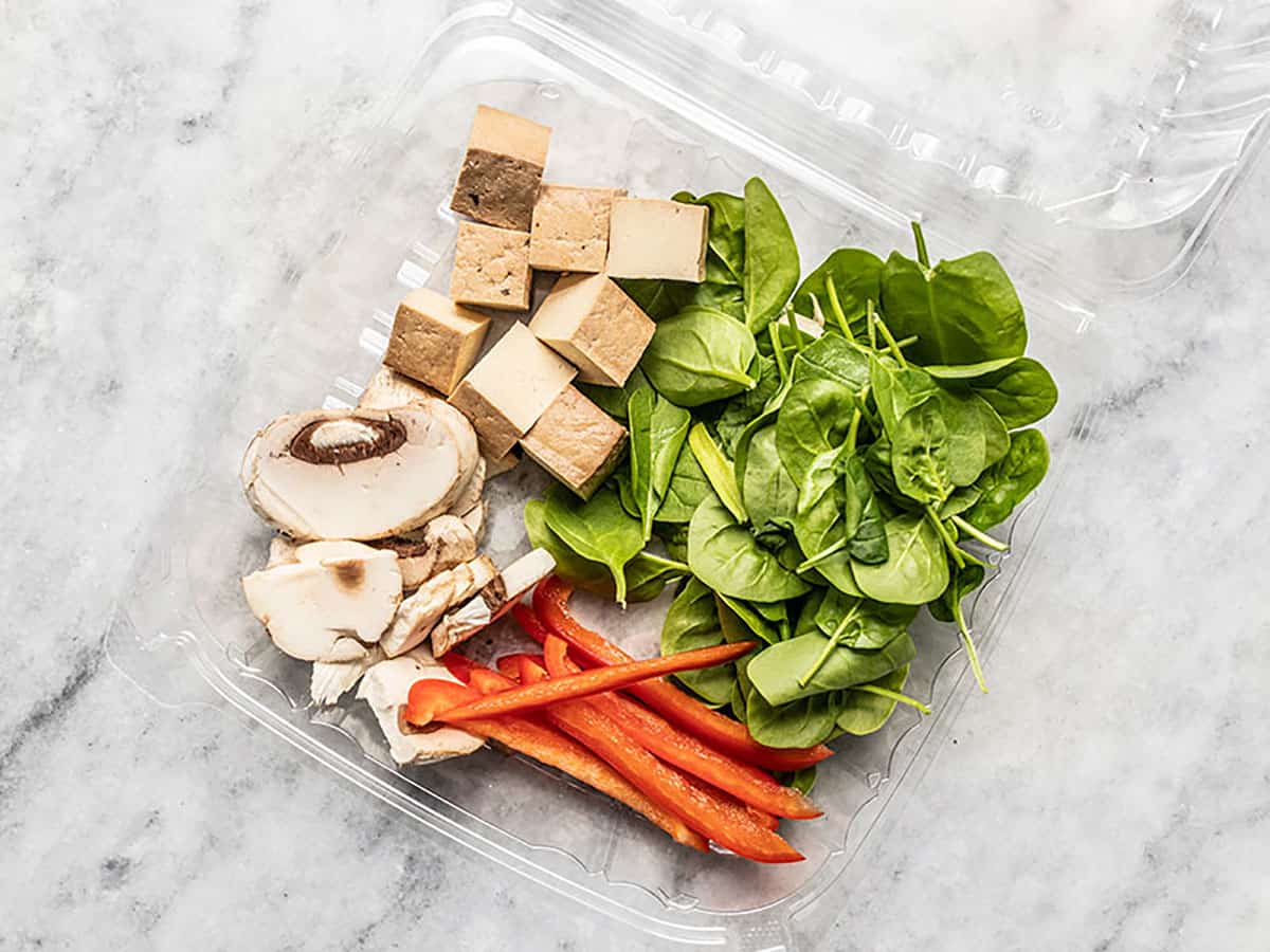 Take out salad bar container with chopped vegetables and tofu cubes.