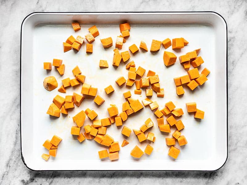 Cubed sweet potatoes on a baking sheet, coated in oil, and ready to be roasted.