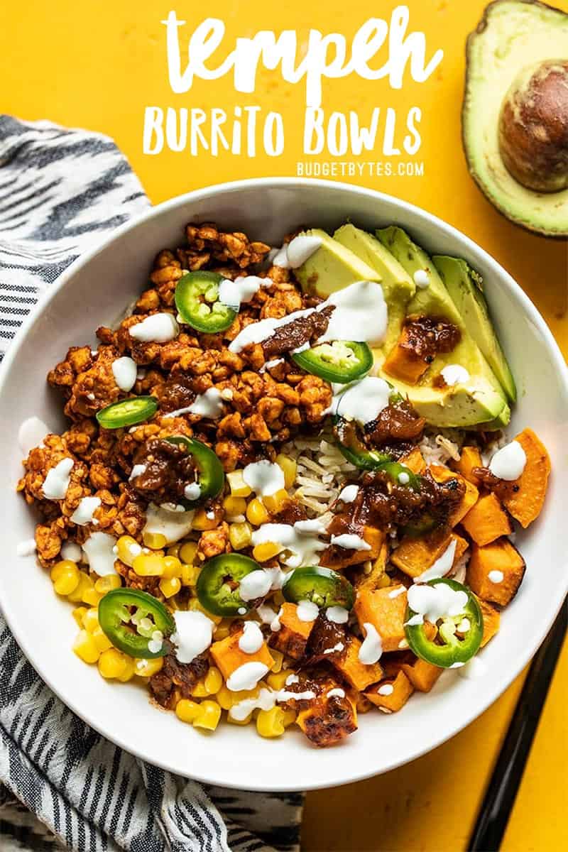 Close up overhead view of a Tempeh Burrito Bowl on a yellow background and an avocado on the side.