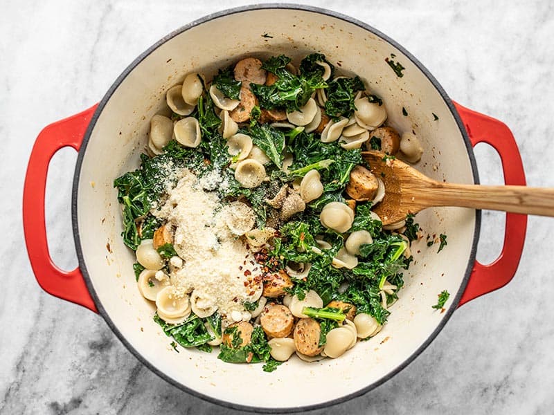 Orecchiette stirred into kale and sausage, Parmesan and pepper added on top.