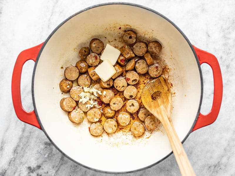 Browned chicken sausage in the pot with minced garlic and butter