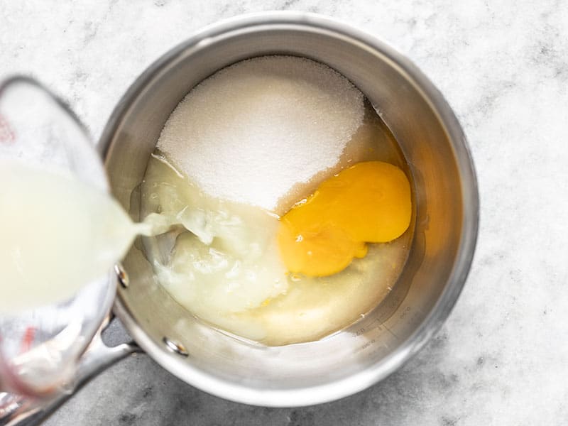 Lemon juice being poured into a sauce pot with sugar and an egg.