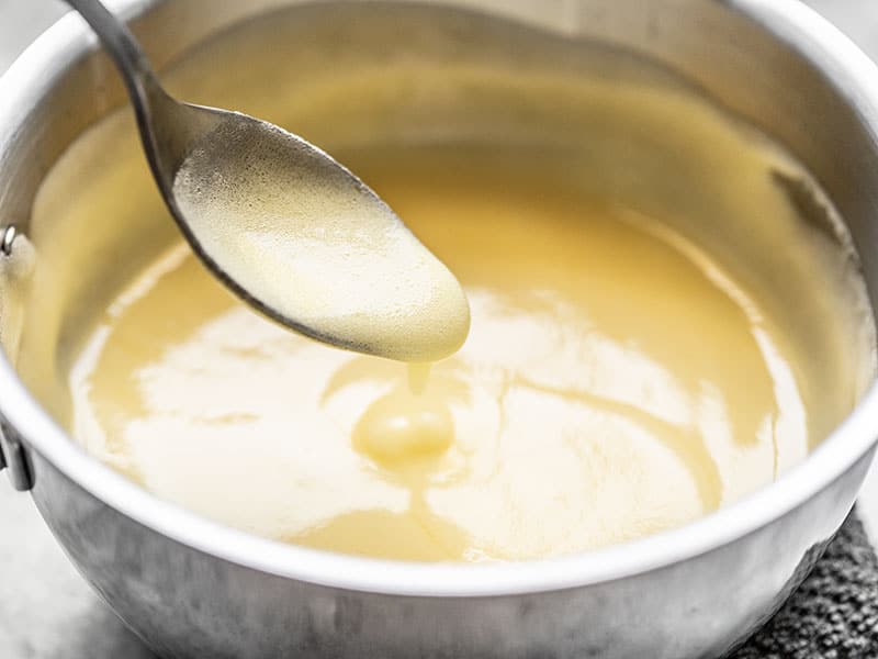 Thickened sugar egg and lemon mixture close up from the side, running off a spoon.