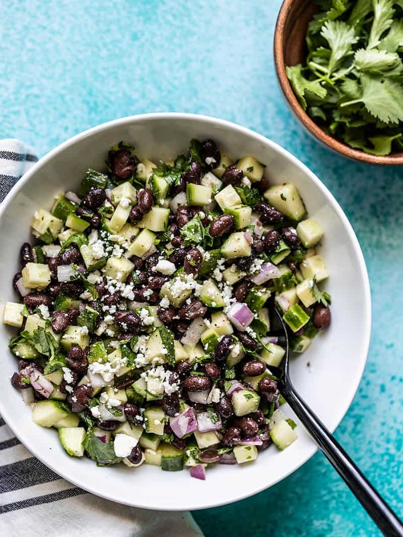 Cucumber and Black Bean Salad in a white bowl with a bowl of cilantro on the side.