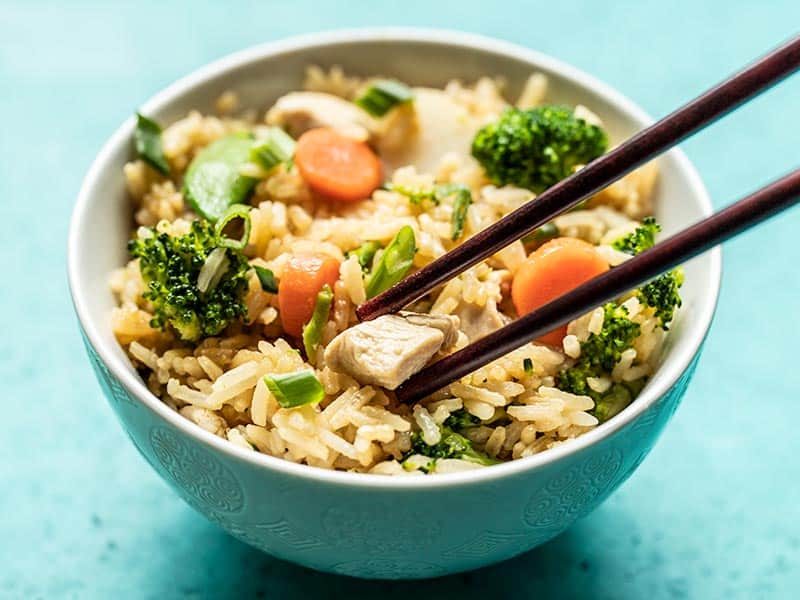 A piece of chicken being picked up by chopsticks out of a bowl of Teriyaki Chicken and Rice