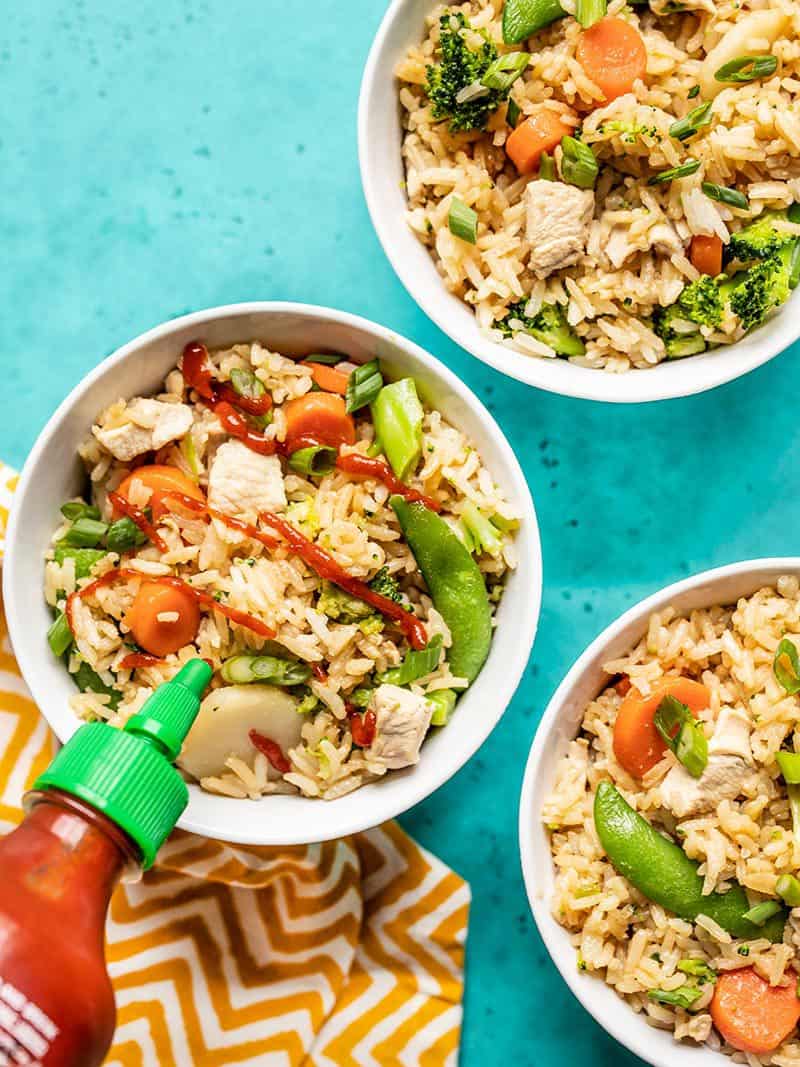 Three bowls of One Pot Teriyaki Chicken and Rice, one with sriracha being drizzled on top.