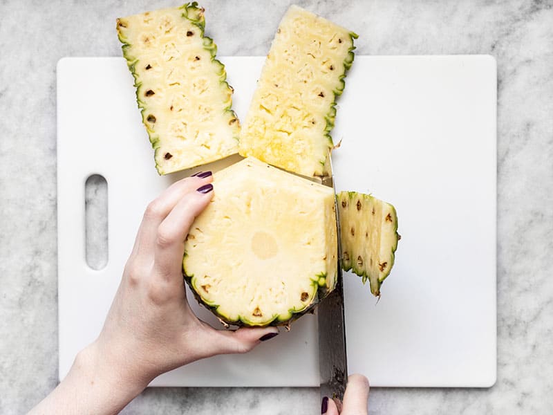 The exterior of the pineapple being cut off as the pineapple stands on end.