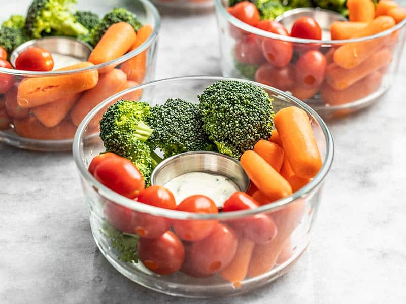 Front view of glass bowl veggie snack packs with ranch dressing, broccoli, carrots, and tomatoes. 