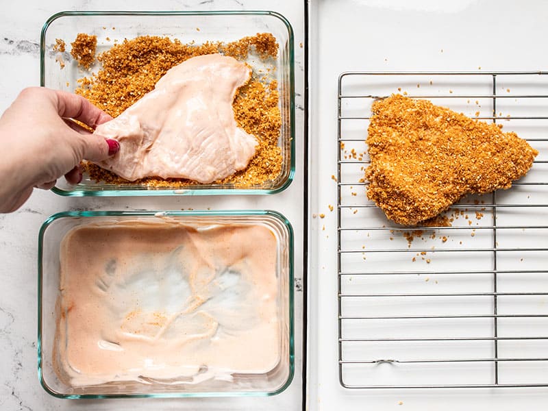 Chicken breast being breaded next to one already breaded piece of chicken.